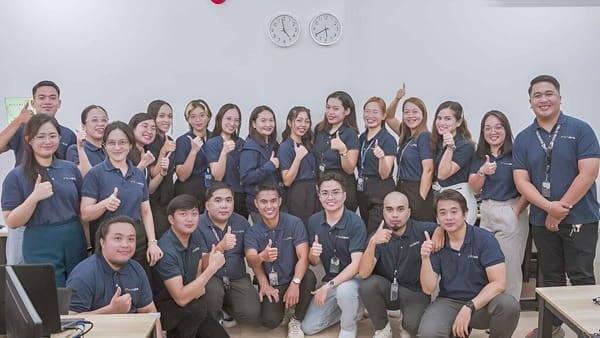 Outdesk team members in a large group smiling at the camera with thumbs up